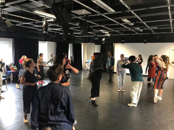 A standing group of people participating in a studio with large windows and black curtains.