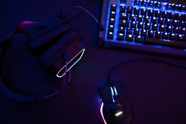 A computer keyboard, mouse and headphones with neon backlights.