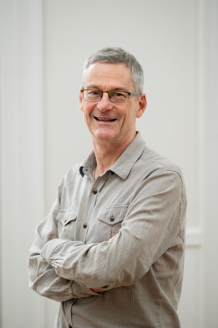 A man in a grey shirt smiles for the camera against a white background