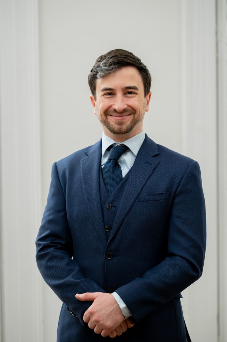 A man in a blue suit smiles for the camera against a white background