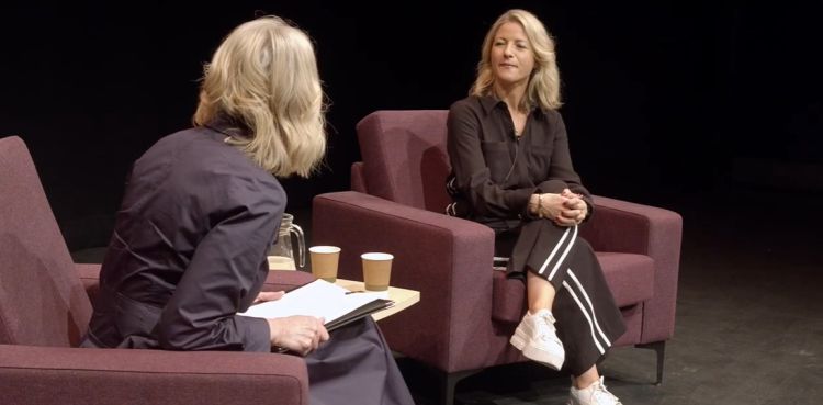 Two women in armchairs on stage, in discussion