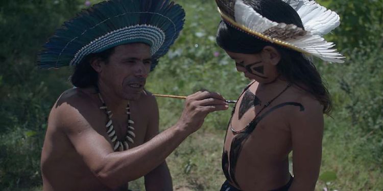 indigenous dressed man applying paint to child's chest