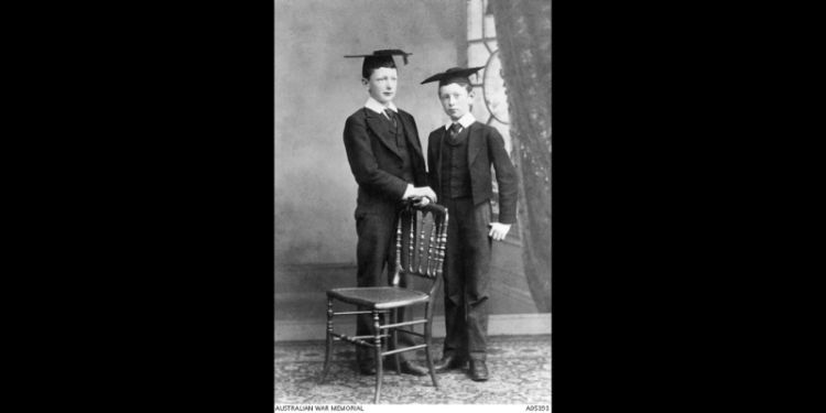 A black and white photograph showing two young boys in suits and wearing mortarboards