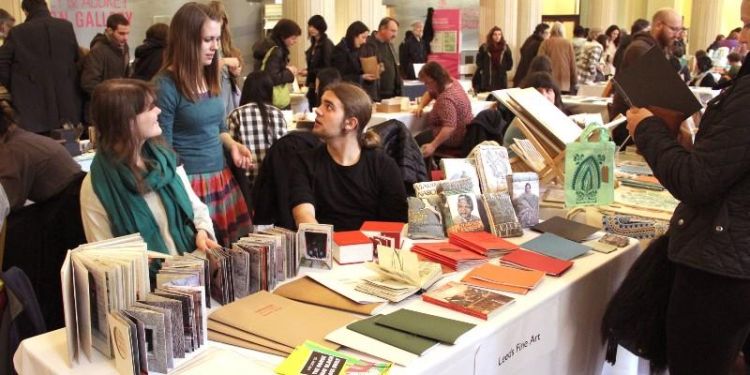 Fine art students next to a table in Parkinson Court. On the table are a range of different artists&#039; books.