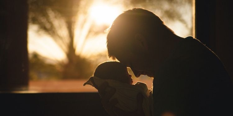 Close-up silhouette of a parent holding a baby with sunset behind.