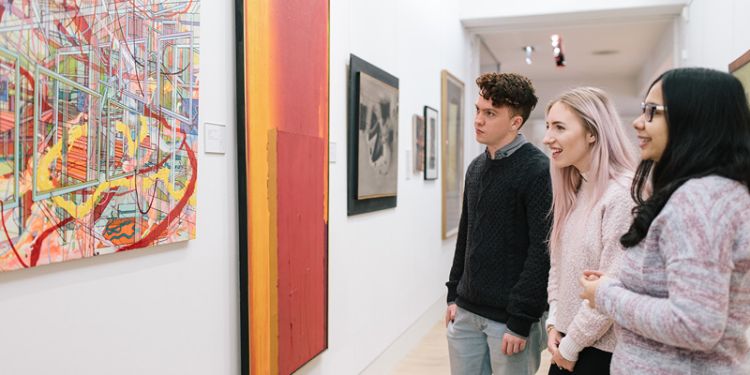 Three people looking at a piece of art on a canvas in a gallery.