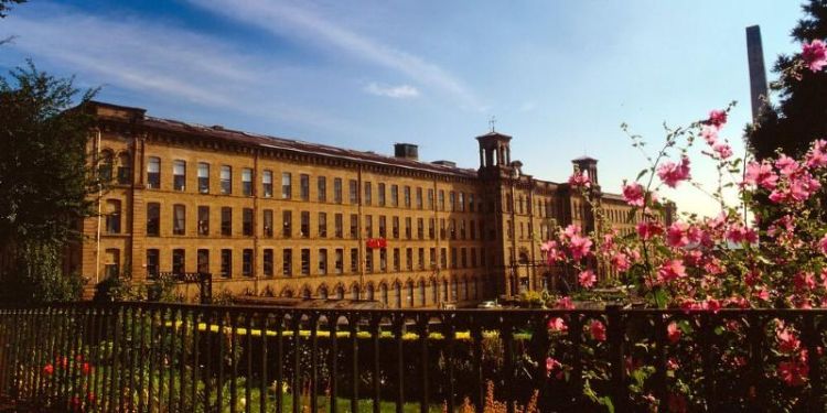 Salts Mill in Saltaire, with the allotments, fence and tree with blossom to the fore