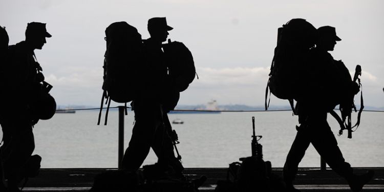 Silhouette of 3 soldiers marching with backpacks.
