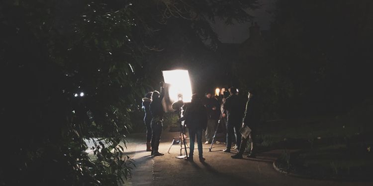 A film crew shooting at night in front of a large spotlight