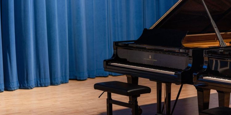 School of Music pianos in the Clothworkers Centenary Concert Hall. The piano and seat are positioned in front of blue velvet drapes.