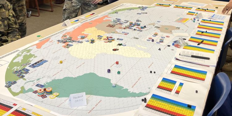 A large war game set up on a table. It shows a map of the world, counters, and printed pages around the edge.