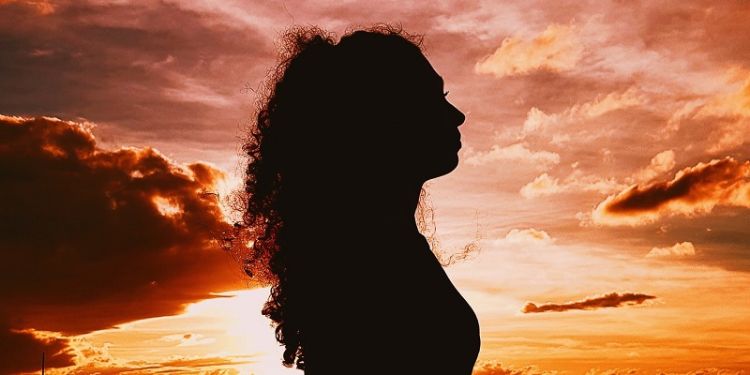 A silhouette of a woman against a fiery sunset