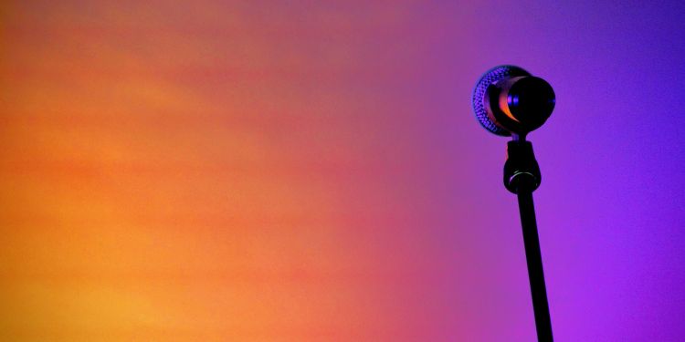 A microphone on a stand in front of an orange and purple gradient background.