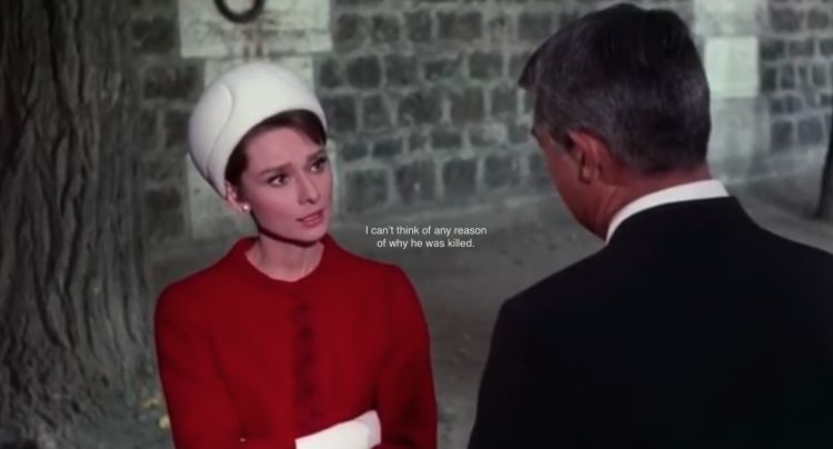 A screenshot from a film showing a woman in red and a man in a black suit, with subtitles on the front of the image