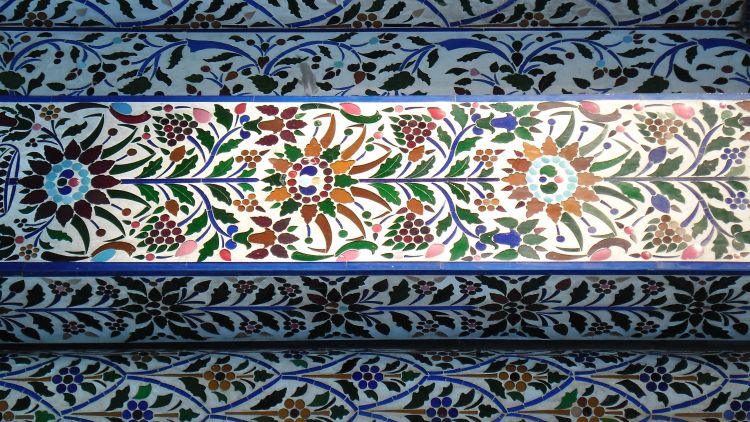 Floor or wall covering pattern of red, orange and green petals and leaves with blue flower stalks.