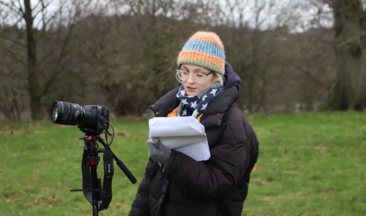 Artist Astrid Butt reading a script next to a camera at Yorkshire Sculpture Park