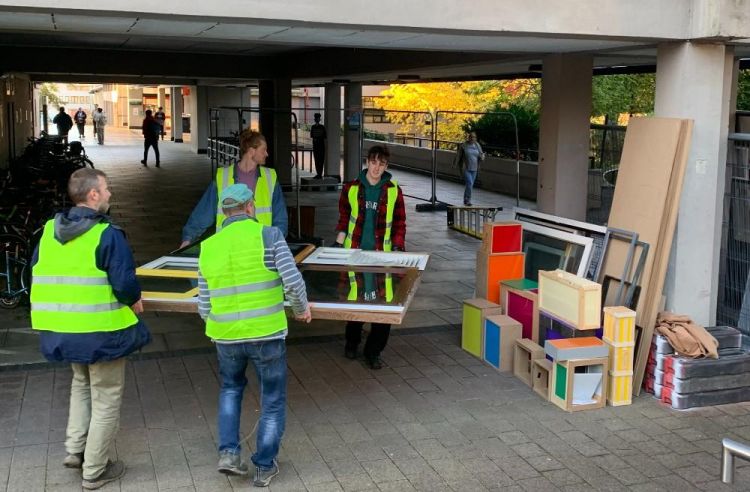 Four people move an art installation by Ed Green into position under cover of a building on the University of Leeds campus.