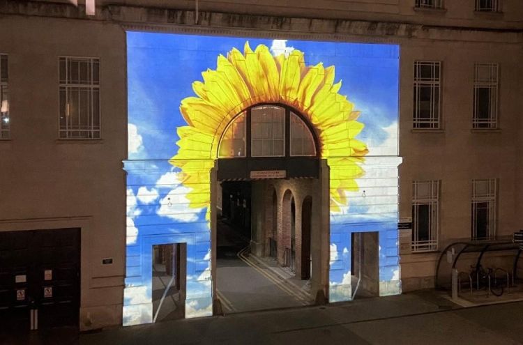 Light projection of a sunflower and sky on a building at night