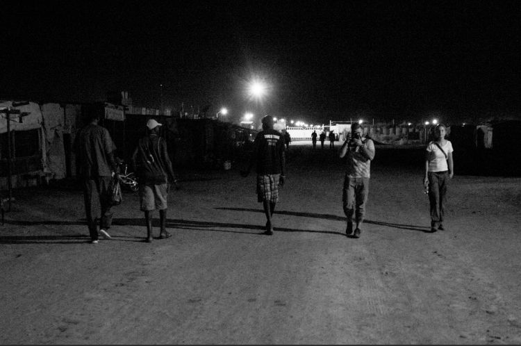 A photographer on a dark road points his lens at the viewer