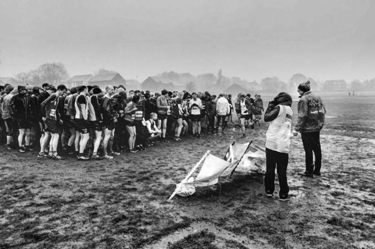 Black and white photograph of athletes grouped together on a muddy sports pitch