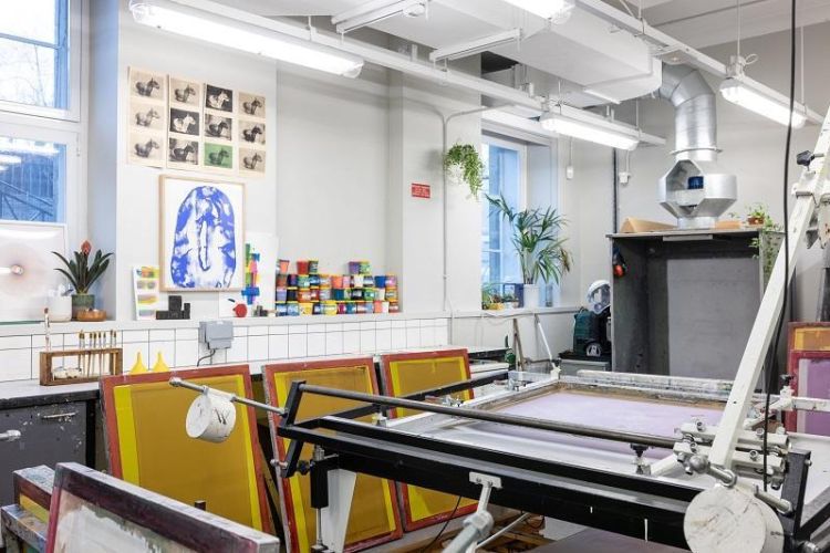 Printmaking workshop in the School of Fine Art, History of Art and Cultural Studies showing screens and other equipment. On the wall are prints made by students and a variety of colours of ink in pots.