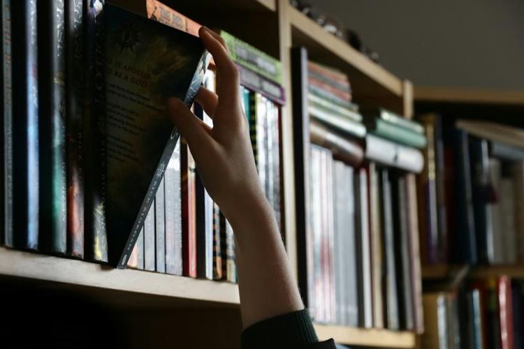 Hand taking a book from a bookshelf