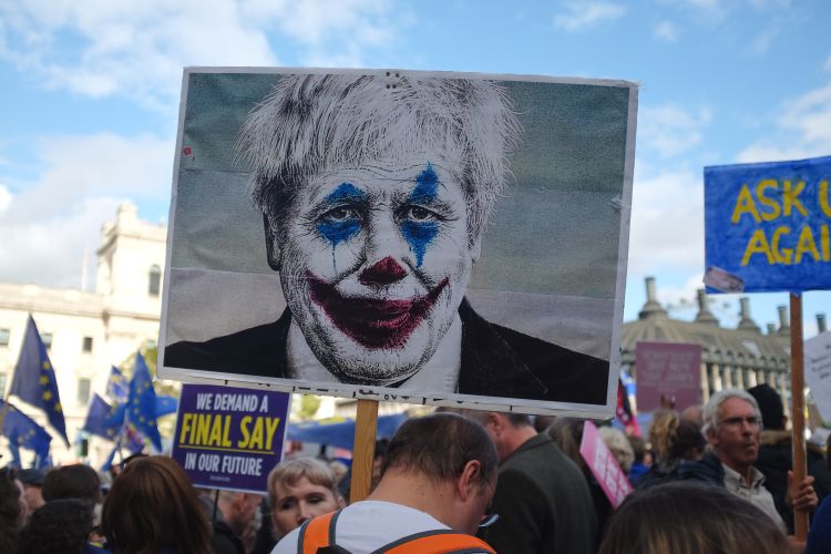 Political protest; protester holding sign with depiction of Boris Johnson in clown makeup