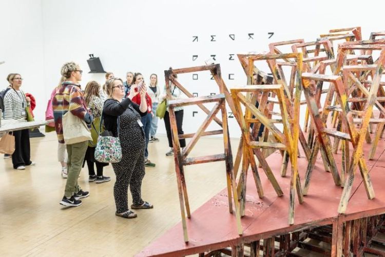 A group of people in an art gallery next to an art installation created with chairs