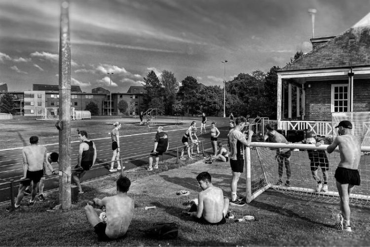 Athletes and spectators next to a running track and grassed area with football goal nets