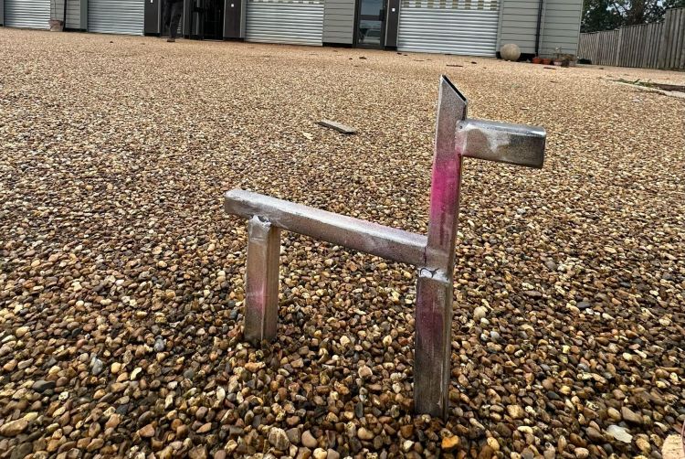 Silver llama sculpture on a pebbled surface with buildings in the background.