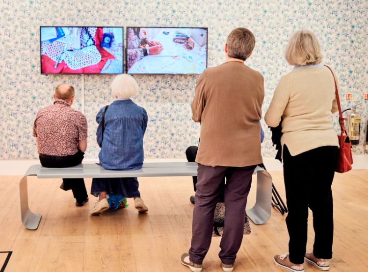 Four people in an art gallery watch a video installation by artist Kalisha Piper-Cheddie.