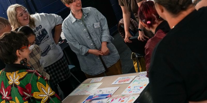 A smiling group of people. They are standing around a table with posters on it