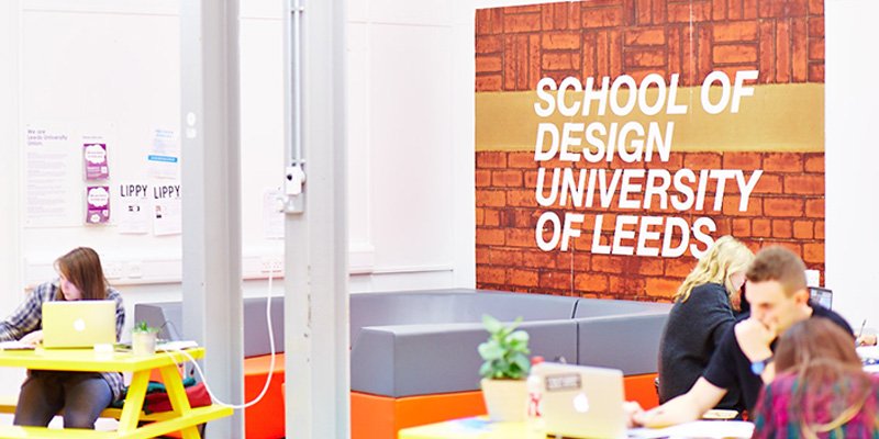 School of Design sign in the common room, surrounded by students working at picnic style tables.