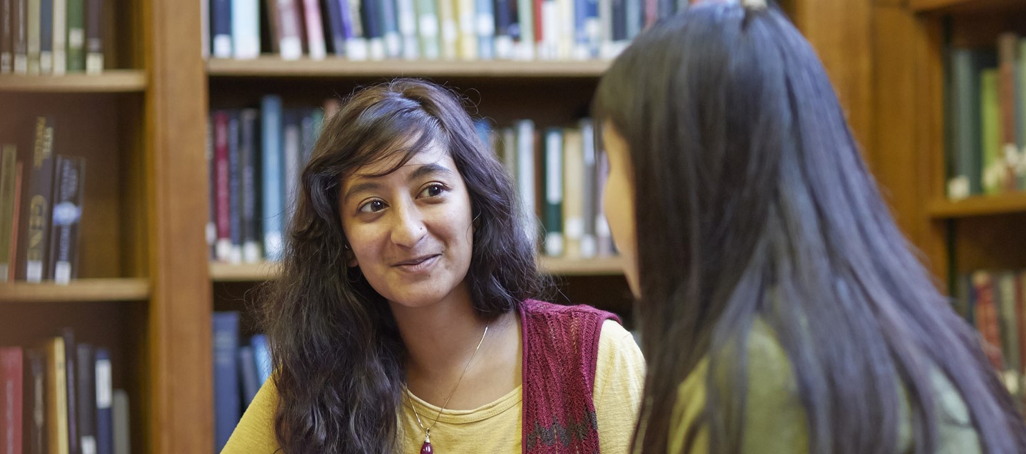indian student sat in the library talking in discussion with a student