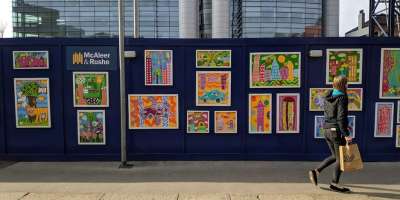 Person walking in front of a building site hoarding which is covered in colourful artwork.
