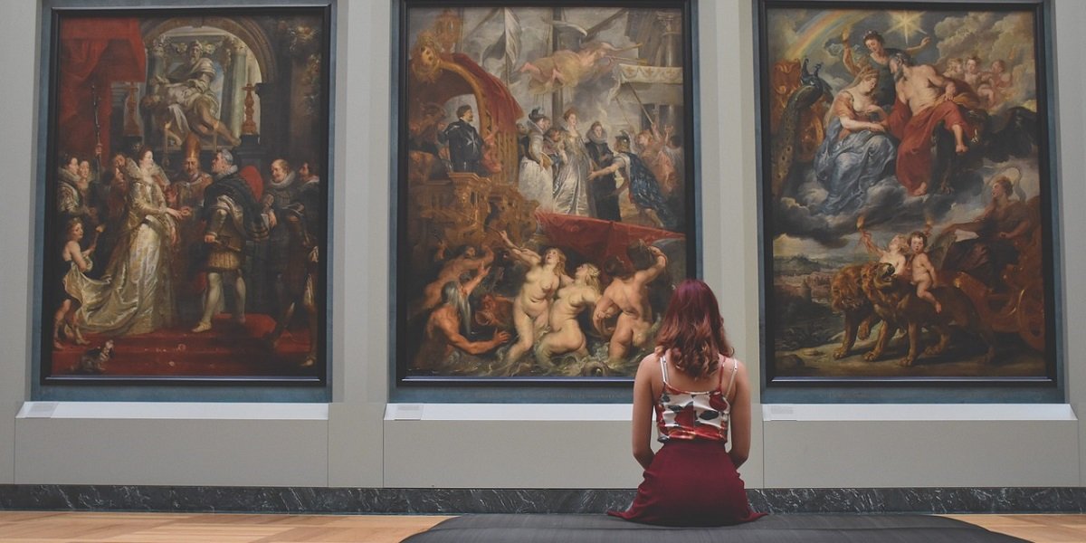 Seated woman looking at three large paintings in a gallery