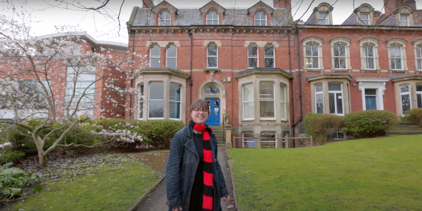 A screenshot from the School of English tour video, a student stands outside the School building about to begin the tour.