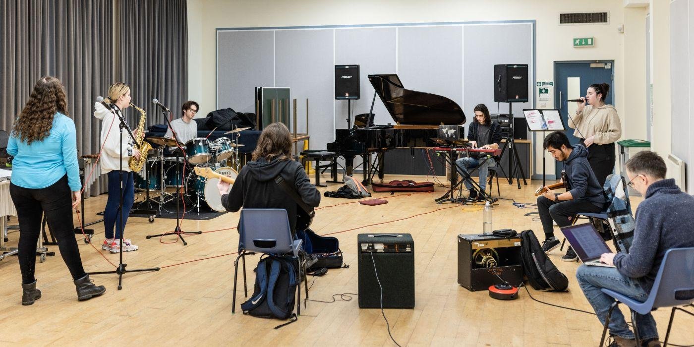 BA students who are part of the School of Music's Band Project performing in the Rehearsal Hall. Some are playing instruments and others singing.