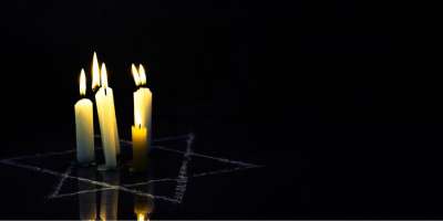 Five, lit white candles in placed in a white star of David against a black background.