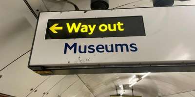Overhead sign in the London Underground with the words way out next to an arrow and the word museums underneath