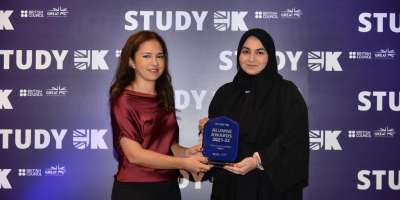 Alumna Dana Al-abduljabbar is pictured receiving a trophy from a presenter. In the background there is a British Council Study UK branded backdrop.