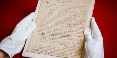 An image of an original Brontë manuscript page held carefully in gloved hands.
