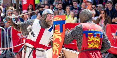 Two people dressed as English knights. One has their shield raised and the other has their sword raised.