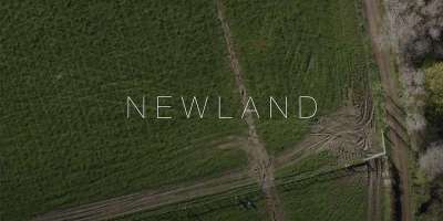 A birds-eye view shot of the farm that features in the film with the film title 'Newland' across the screen.