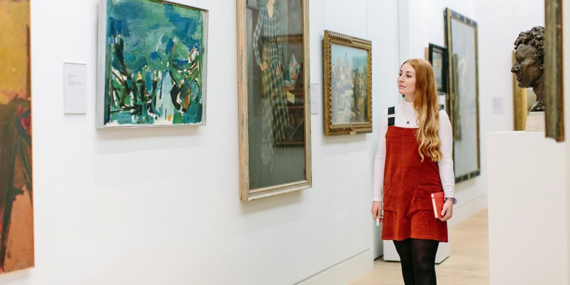 Student walking through a gallery with paintings hung on the walls.