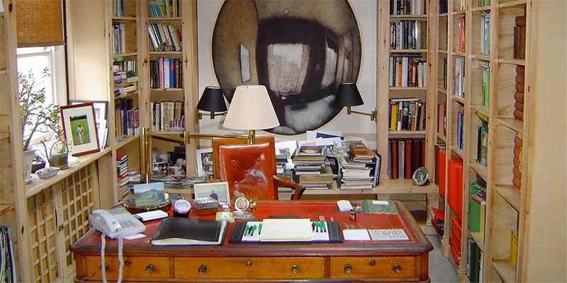 A view of Harold Pinter's writing desk. There are many books stacked around the walls.